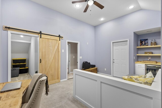 home office with beverage cooler, a ceiling fan, light colored carpet, and a barn door