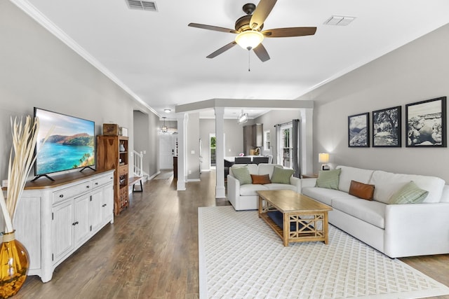 living area with dark wood-style flooring, ceiling fan, baseboards, visible vents, and ornamental molding