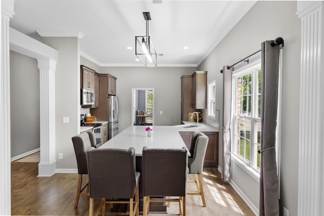 dining area with ornate columns, baseboards, crown molding, and light wood-type flooring