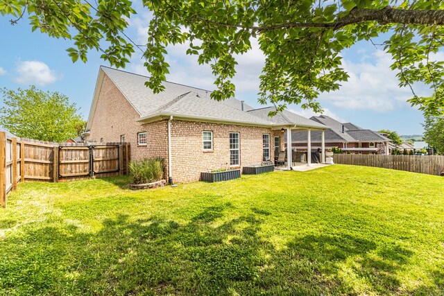 rear view of house featuring brick siding, a fenced backyard, a yard, and a patio