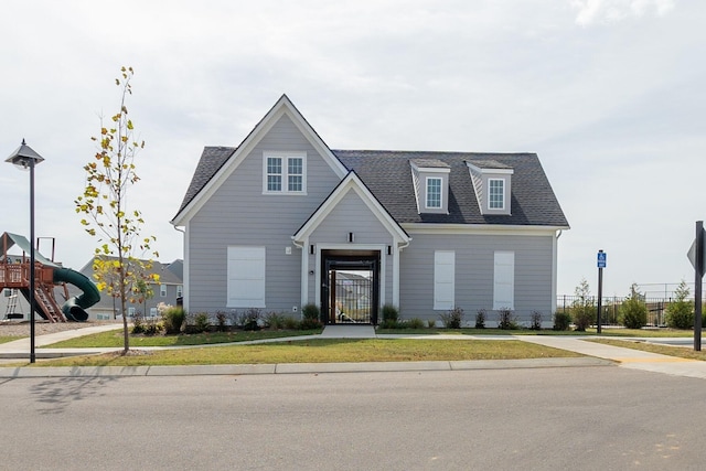 view of front facade with a playground, roof with shingles, and a front yard