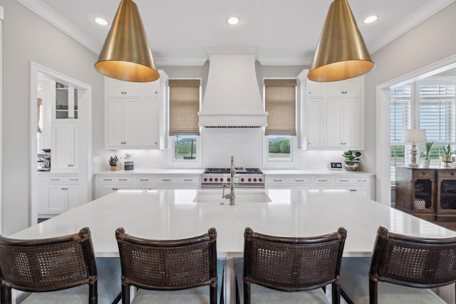 kitchen with crown molding, stainless steel range, premium range hood, recessed lighting, and a center island with sink