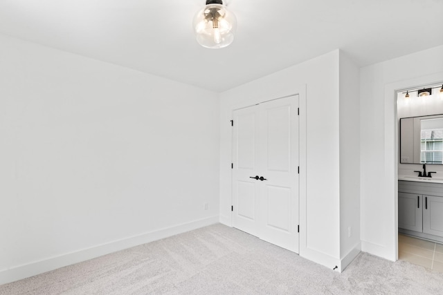 interior space featuring light colored carpet, a sink, baseboards, and ensuite bath