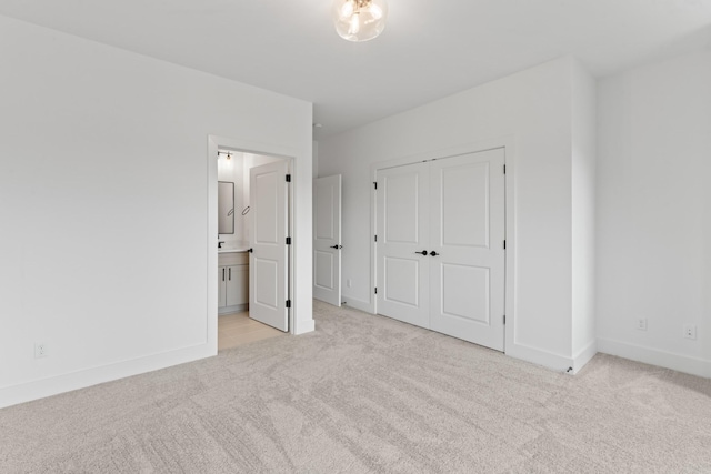 unfurnished bedroom with baseboards, light carpet, a closet, and ensuite bath