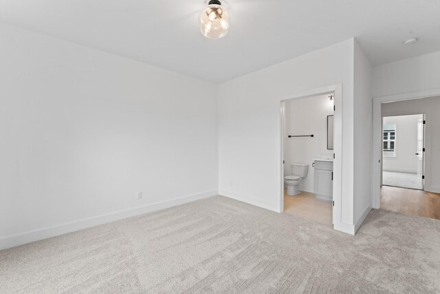 unfurnished bedroom with baseboards, light carpet, and ensuite bathroom