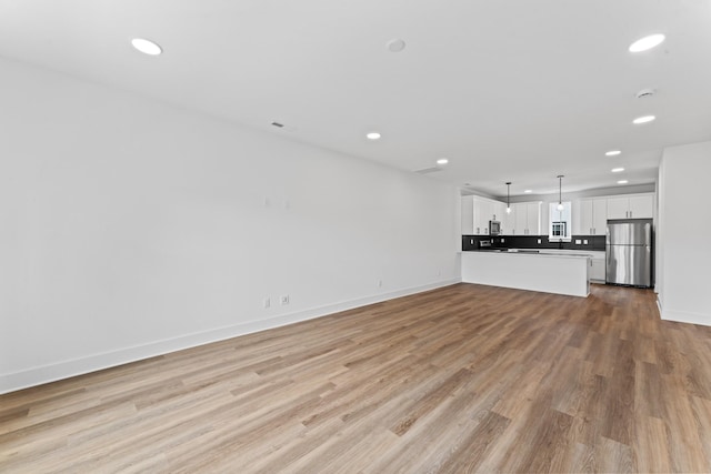 unfurnished living room with baseboards, recessed lighting, and light wood-style flooring