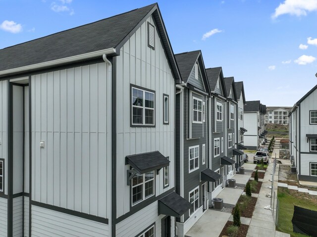 view of property exterior featuring a shingled roof, board and batten siding, a residential view, and cooling unit