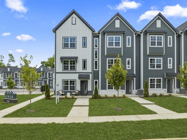 townhome / multi-family property with board and batten siding, cooling unit, and a front yard