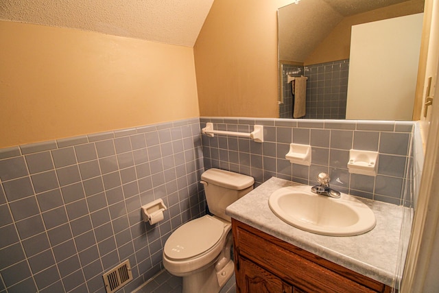 bathroom with a textured ceiling, tile walls, vanity, toilet, and lofted ceiling