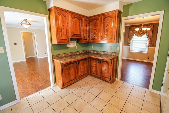 kitchen featuring ornamental molding, dark countertops, light wood-type flooring, brown cabinets, and a notable chandelier