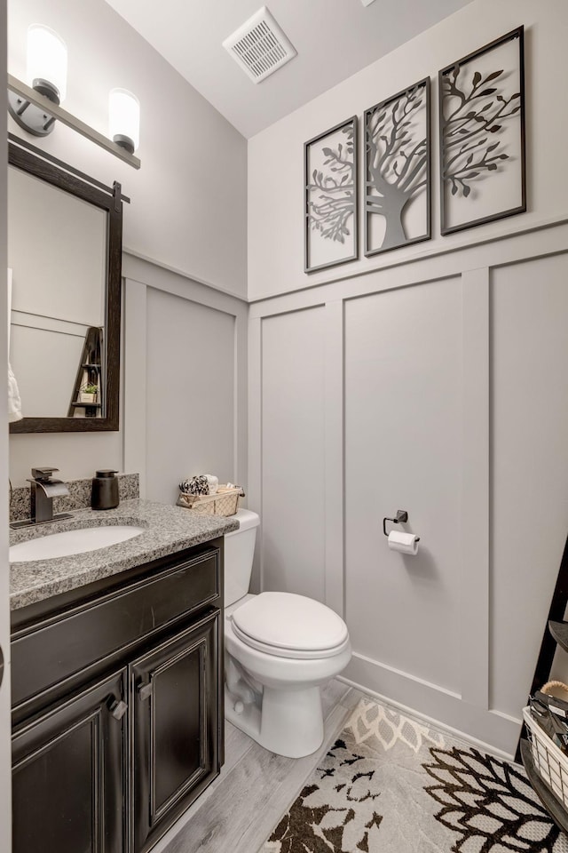 half bathroom with visible vents, wood finished floors, toilet, and vanity