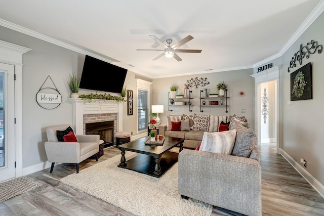 living area featuring crown molding, a ceiling fan, wood finished floors, and a fireplace