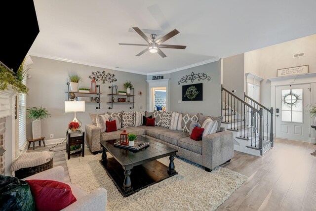 living area featuring visible vents, ornamental molding, stairs, a ceiling fan, and light wood finished floors