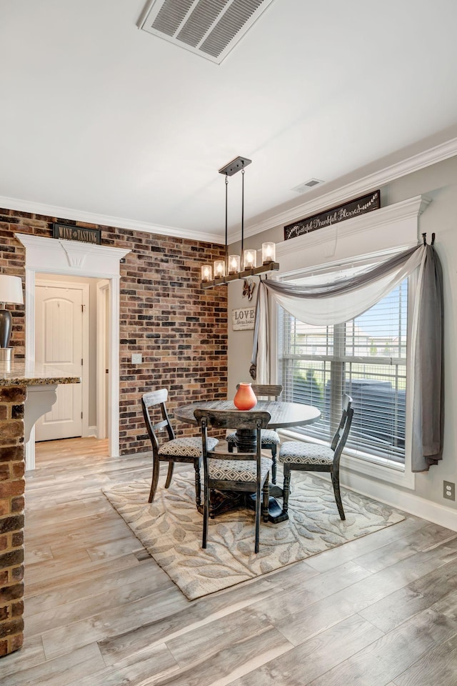 dining space with crown molding, brick wall, visible vents, and light wood-style flooring
