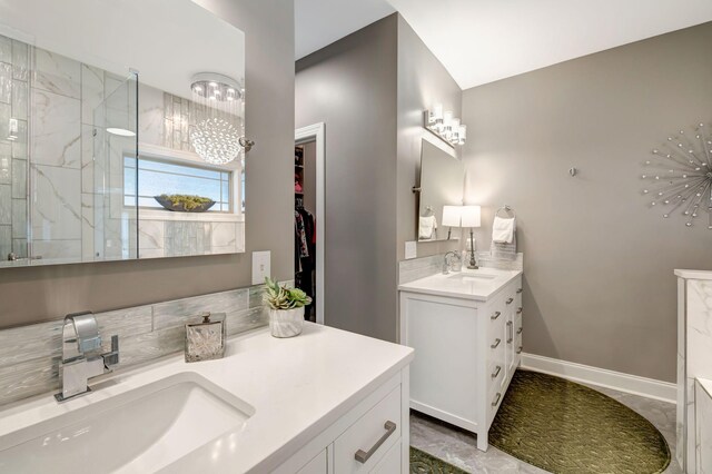 bathroom featuring baseboards, a sink, a walk in shower, and two vanities