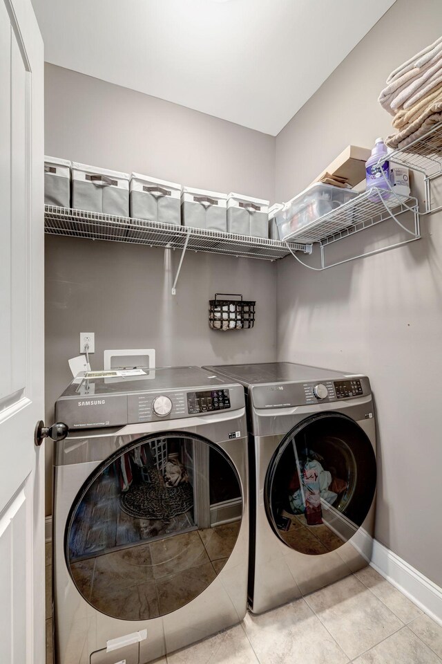 clothes washing area featuring laundry area, tile patterned floors, baseboards, and washing machine and dryer