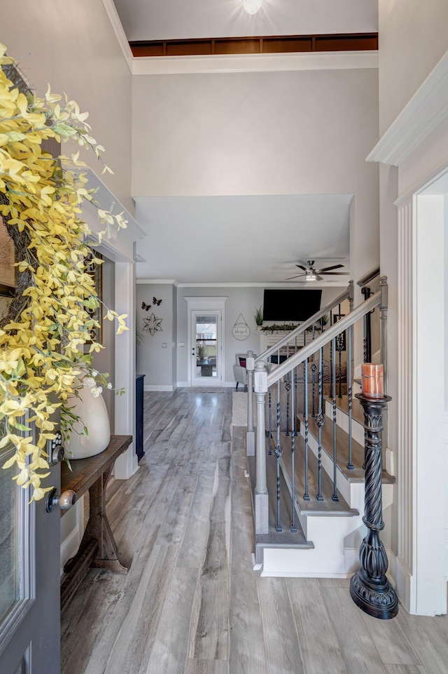 foyer entrance with crown molding, wood finished floors, a high ceiling, stairway, and a ceiling fan