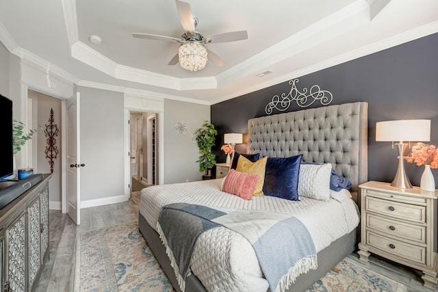 bedroom with crown molding, wood finished floors, baseboards, ceiling fan, and a raised ceiling