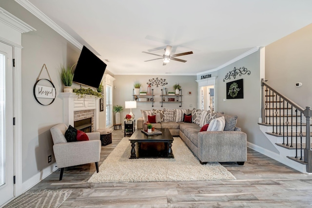 living room featuring a ceiling fan, baseboards, wood finished floors, ornamental molding, and stairway