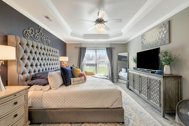 bedroom featuring a raised ceiling, a ceiling fan, light wood-type flooring, visible vents, and ornamental molding
