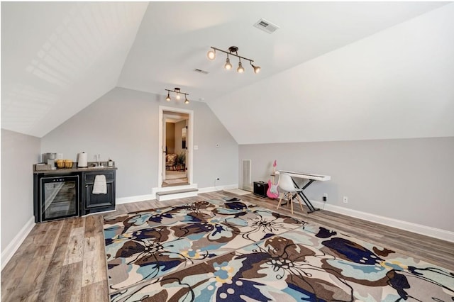 additional living space featuring beverage cooler, baseboards, wood finished floors, lofted ceiling, and visible vents