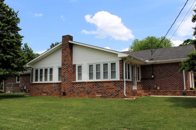 view of property exterior featuring a chimney, a yard, central AC, and brick siding