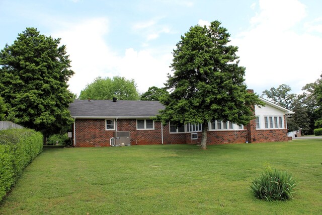 rear view of house with brick siding, central AC unit, a yard, and a chimney