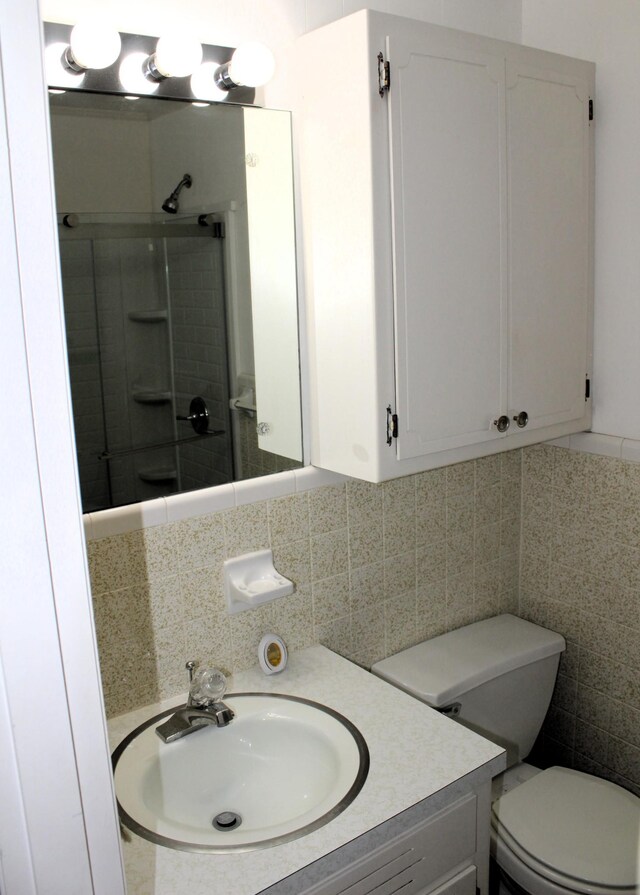 bathroom featuring a shower with shower door, vanity, toilet, tile walls, and backsplash