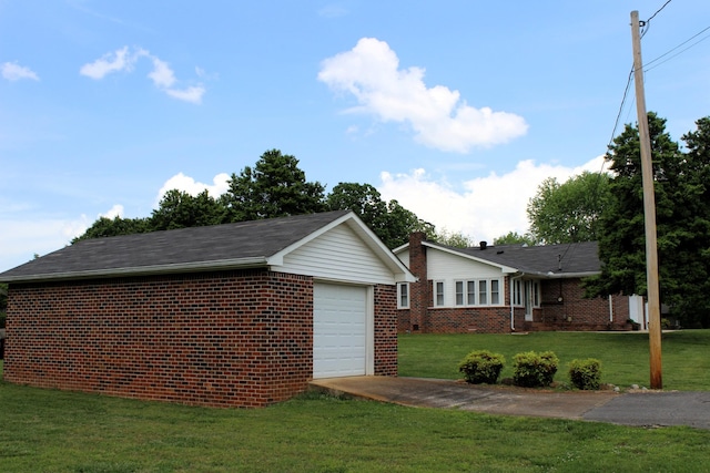 view of side of property with driveway, a lawn, a garage, brick siding, and an outdoor structure