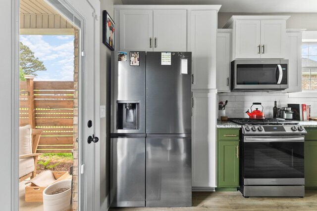 kitchen with light wood-style floors, green cabinetry, white cabinets, tasteful backsplash, and stainless steel appliances