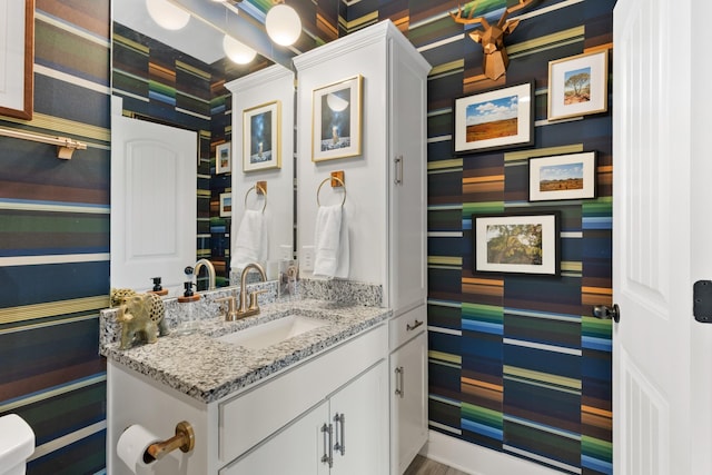 half bath featuring wallpapered walls and vanity