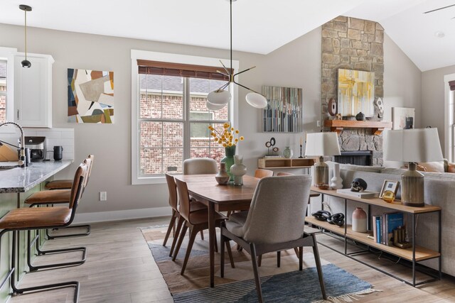 dining area with a stone fireplace, plenty of natural light, light wood-style flooring, and lofted ceiling
