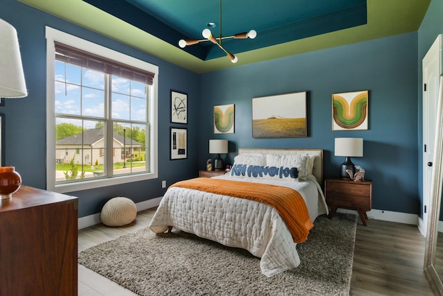 bedroom with a tray ceiling, a notable chandelier, baseboards, and wood finished floors