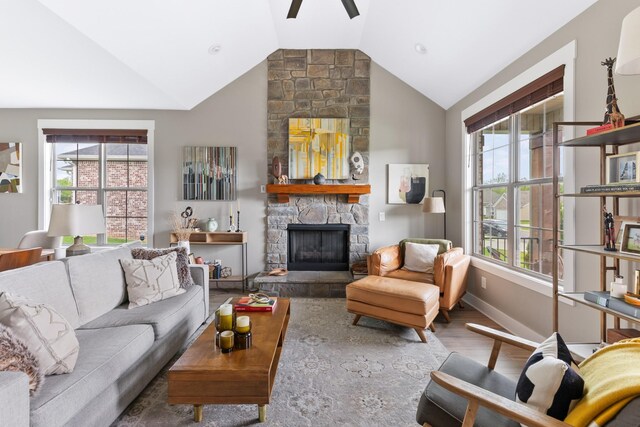 living area featuring wood finished floors, lofted ceiling, baseboards, a stone fireplace, and ceiling fan