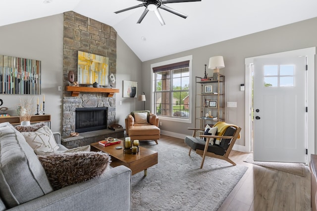 living room featuring ceiling fan, high vaulted ceiling, a stone fireplace, baseboards, and wood finished floors
