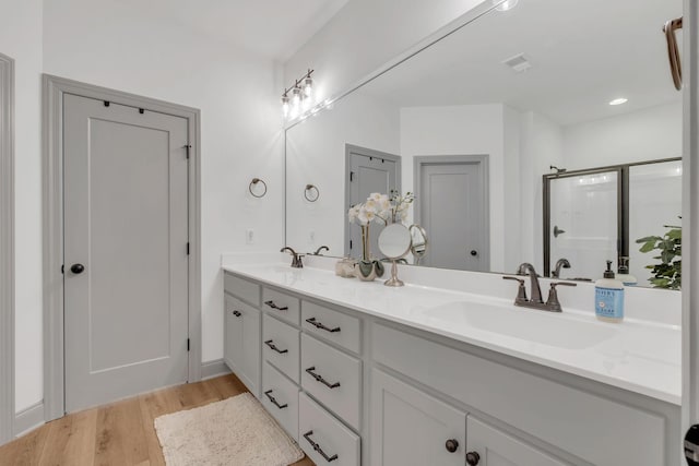 bathroom featuring double vanity, a shower stall, a sink, and wood finished floors