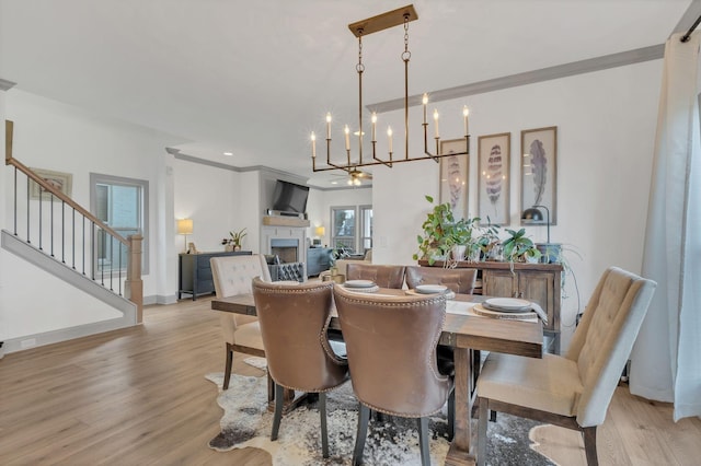 dining space featuring an inviting chandelier, light wood-style flooring, stairs, and a fireplace