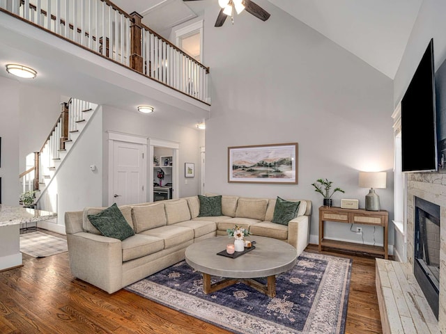 living area with wood finished floors, a fireplace, ceiling fan, stairway, and high vaulted ceiling