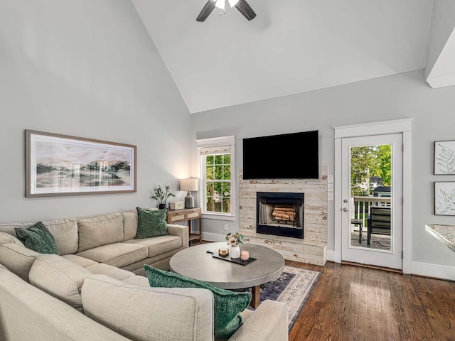 living room featuring a healthy amount of sunlight, ceiling fan, a fireplace with raised hearth, and dark wood-type flooring