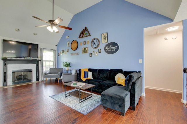 living area with a ceiling fan, wood finished floors, high vaulted ceiling, and a tile fireplace