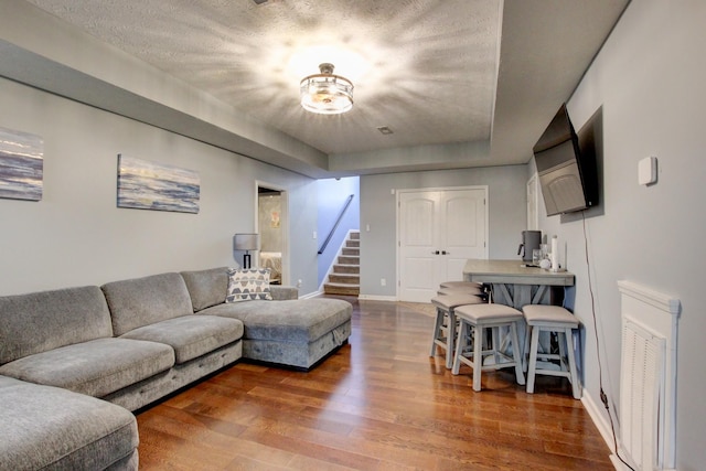 living room featuring a textured ceiling, baseboards, wood finished floors, a tray ceiling, and stairway