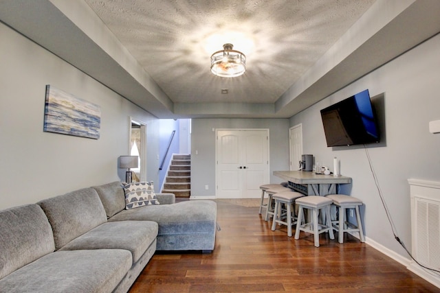 living room with visible vents, wood finished floors, baseboards, stairway, and a raised ceiling