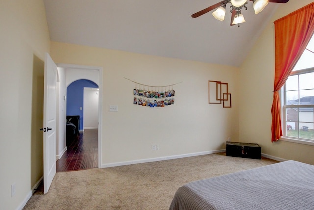 carpeted bedroom with baseboards, arched walkways, ceiling fan, and vaulted ceiling