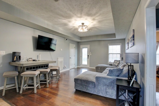 living room featuring a textured ceiling, baseboards, wood finished floors, and a raised ceiling