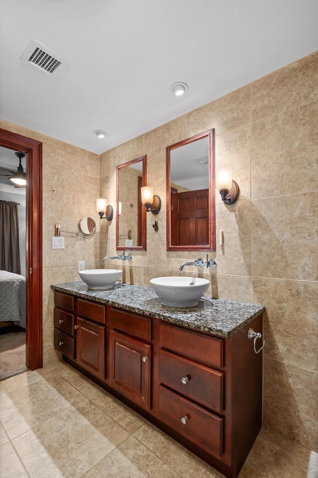 full bath with double vanity, tile walls, a sink, and visible vents