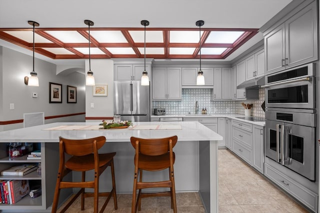 kitchen with a kitchen island, tasteful backsplash, a sink, gray cabinetry, and stainless steel appliances