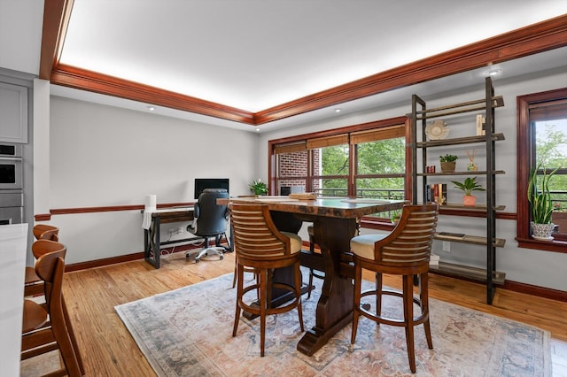dining room with baseboards, a tray ceiling, ornamental molding, and light wood-style flooring