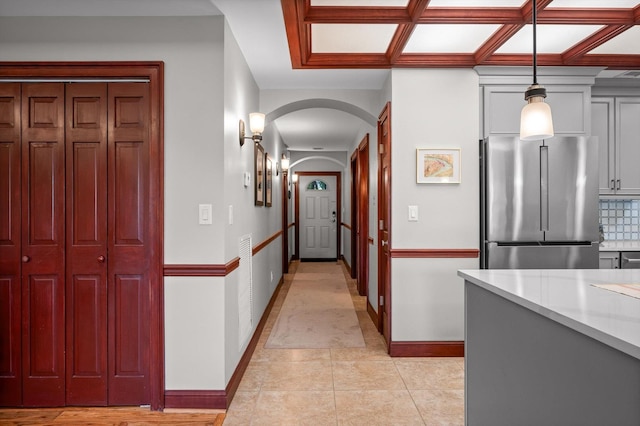 hallway featuring baseboards, arched walkways, coffered ceiling, and light tile patterned floors