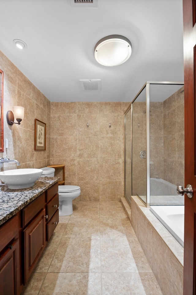 full bath with vanity, a tile shower, toilet, and tile walls