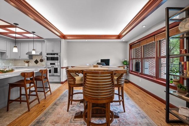 dining area featuring a raised ceiling, baseboards, ornamental molding, and light wood finished floors